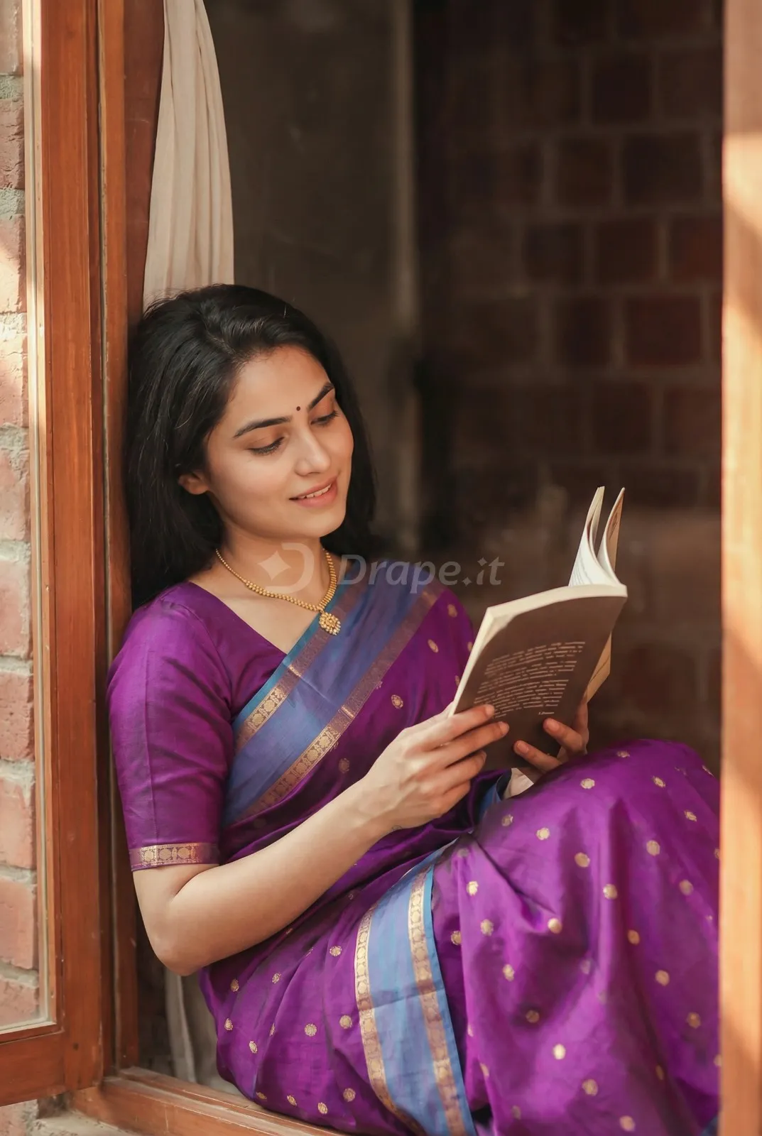 Lifestyle saree photo — model in a purple silk saree reading by a window
